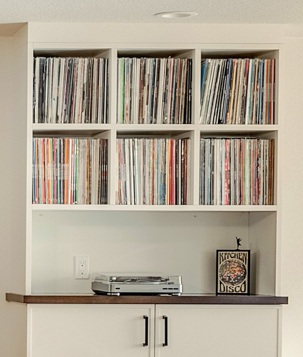Record collection on custom-made cabinet shelves with a turntable and 'Kitchen Disco' plaque in a home setting.