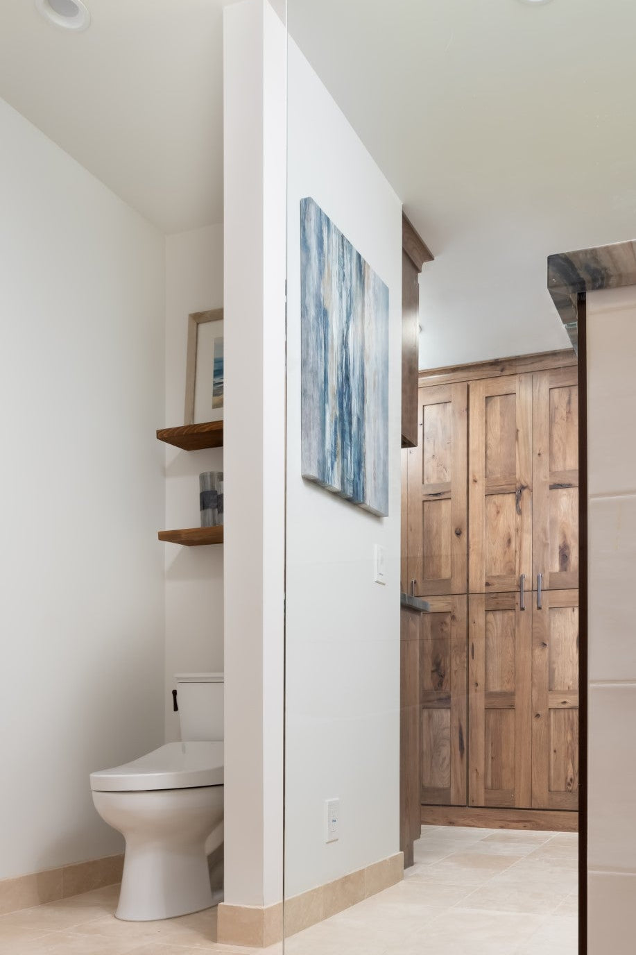 Bathroom interior with private alcove for toilet, tiled floor, wooden cabinet, and shelves.