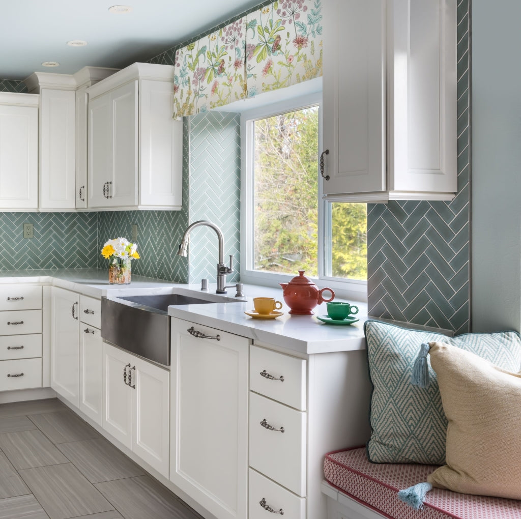 Transitional Kitchen Remodel with custom white cabinets, teal herringbone tile backsplash, built-in window seat with colorful cushion and pillows, and floral window valance