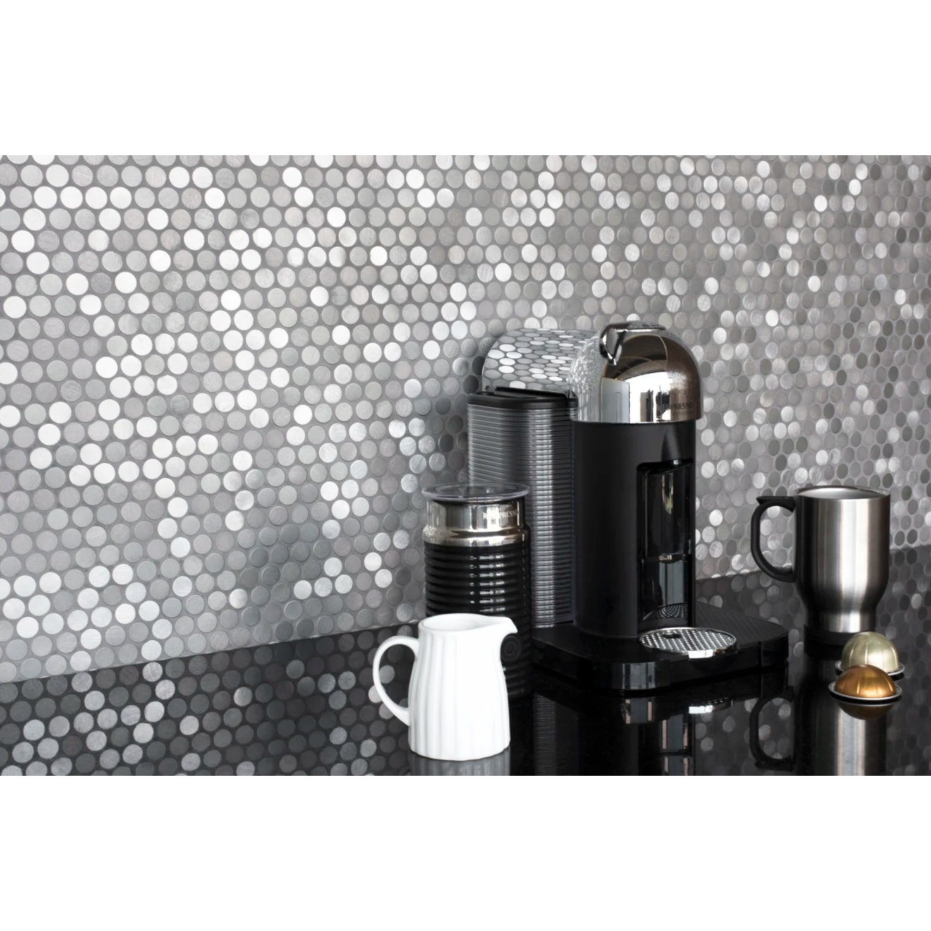 Polished black granite countertop with coffee maker and silver mug placed on top, against Penny round tile in the color Iron. 