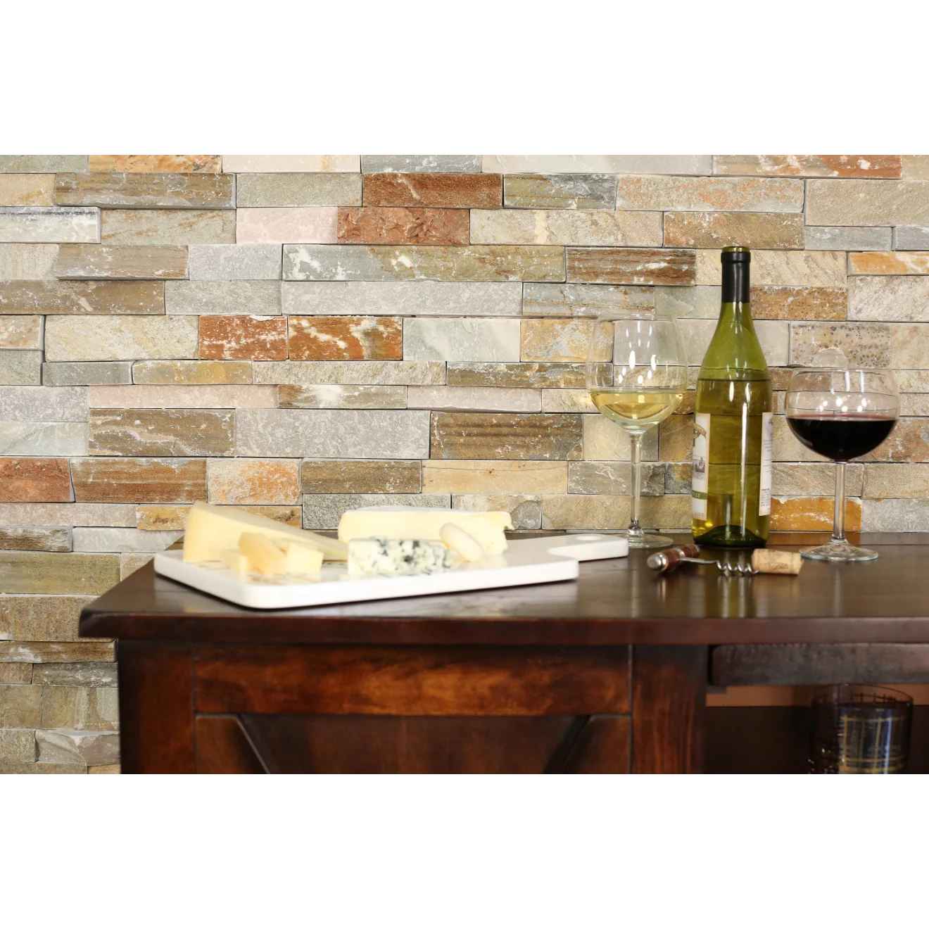 Split-face ledger wall application with a cabinet in front with an open, green, wine bottle, two wine glasses, and a plate of cheese. 