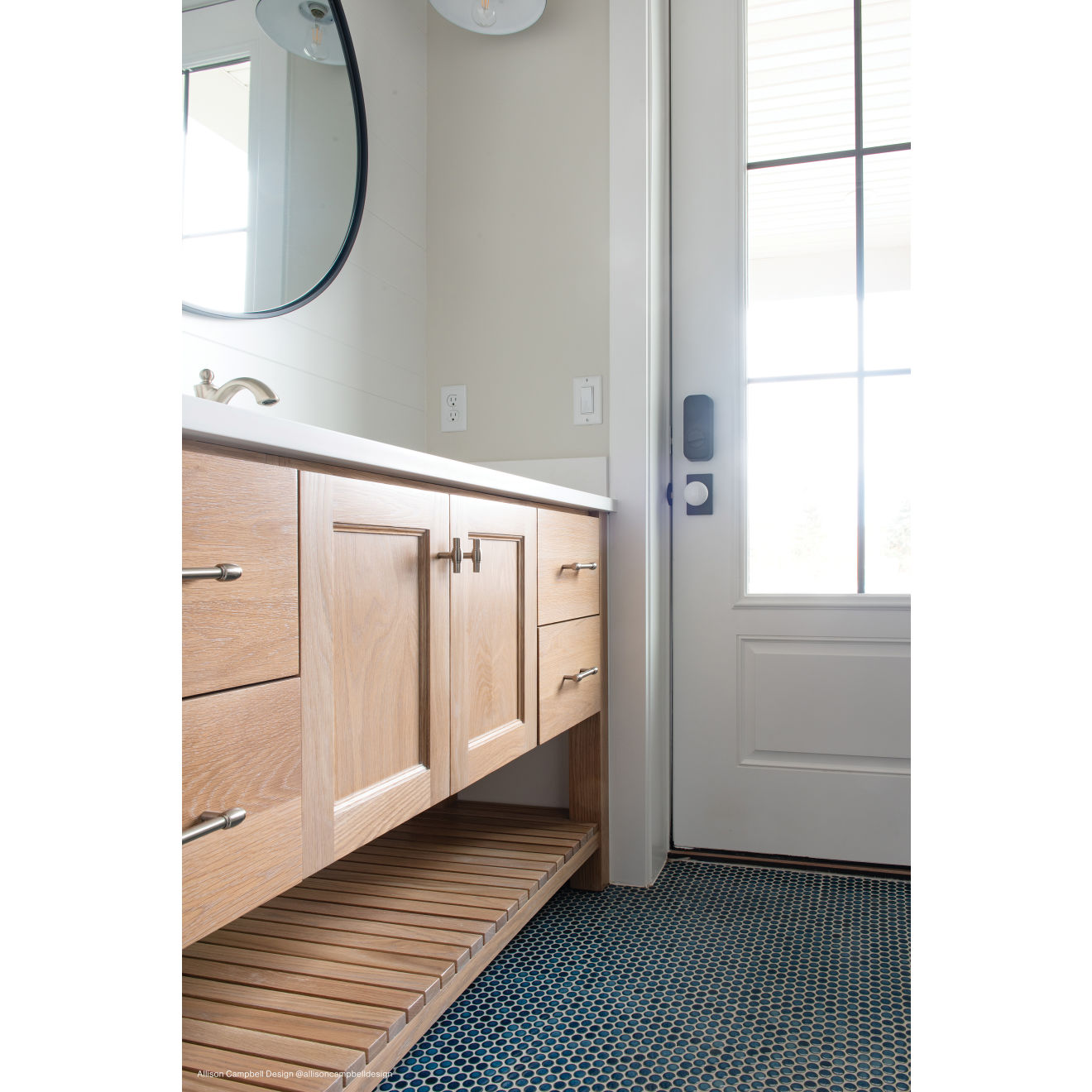 Light brown wooden bathroom vanity on top of a random assortment of matte penny rounds as flooring.