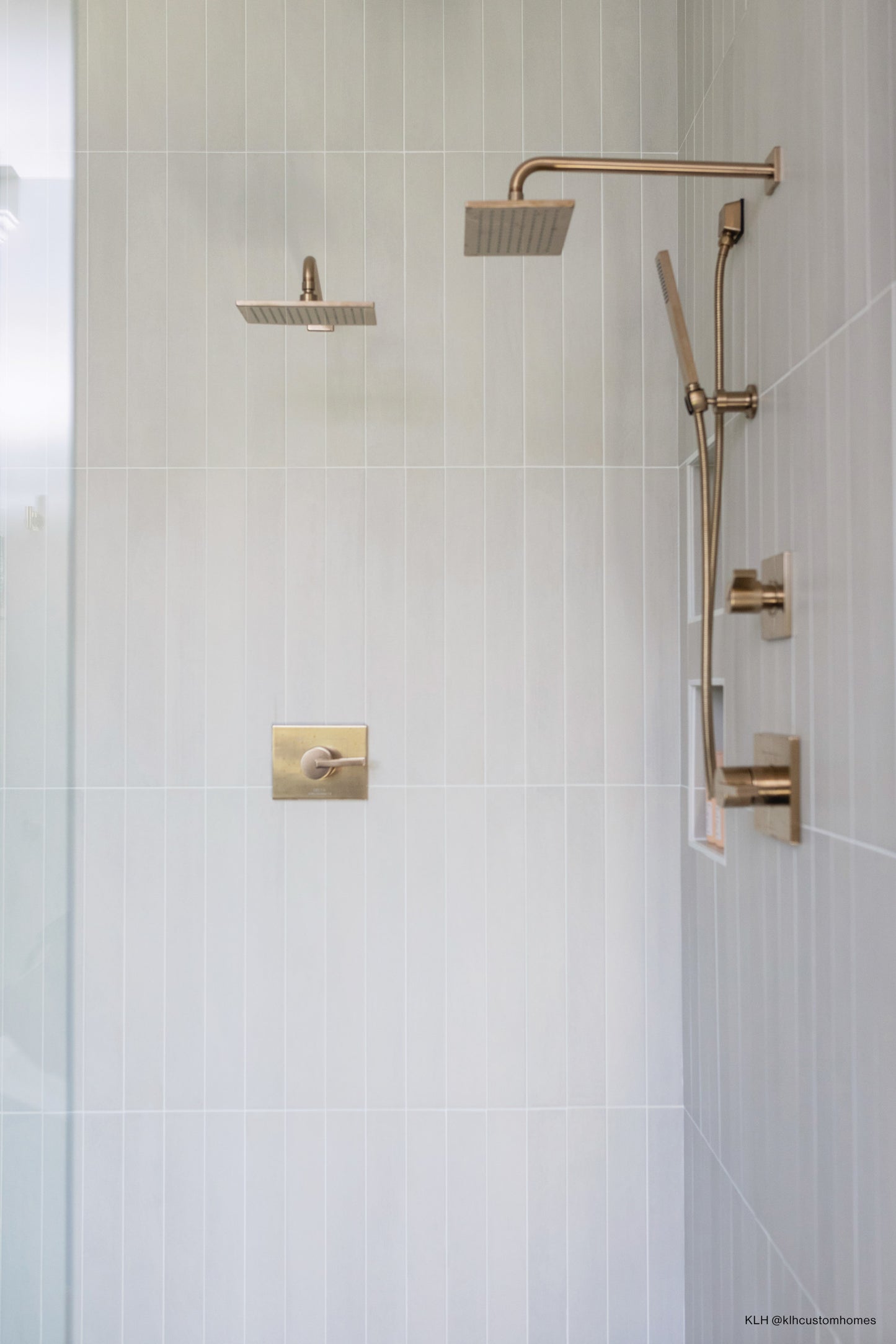 White matte field tile laid vertically on shower wall with gold plumbing and hardware.